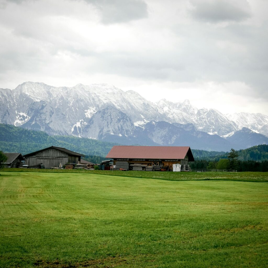 Scenic view of a rustic Bavarian farmhouse set against the dramatic backdrop of snow-capped mountains in Deutschland.
